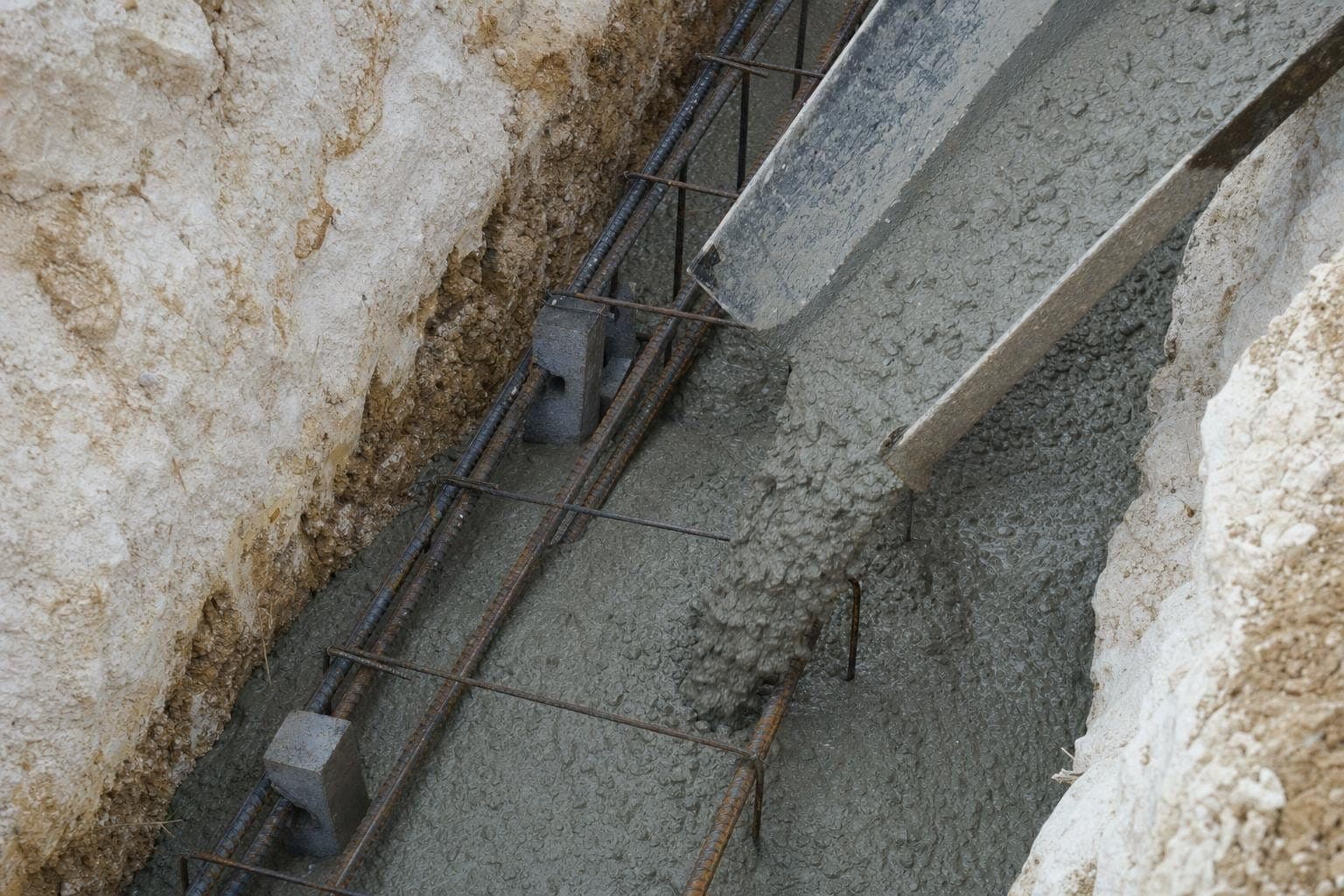 Armatures d'une semelle filante dans une tranchée, béton frais en cours de coulage