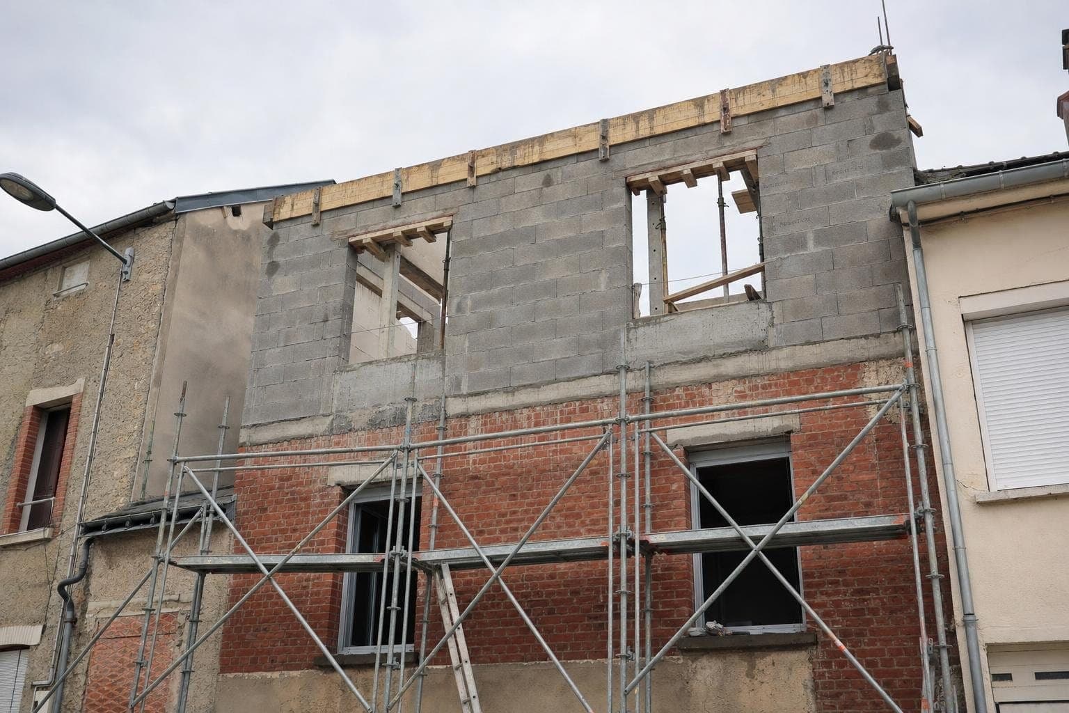 Nouvel étage en blocs béton monté sur une maison en brique, échafaudage en façade