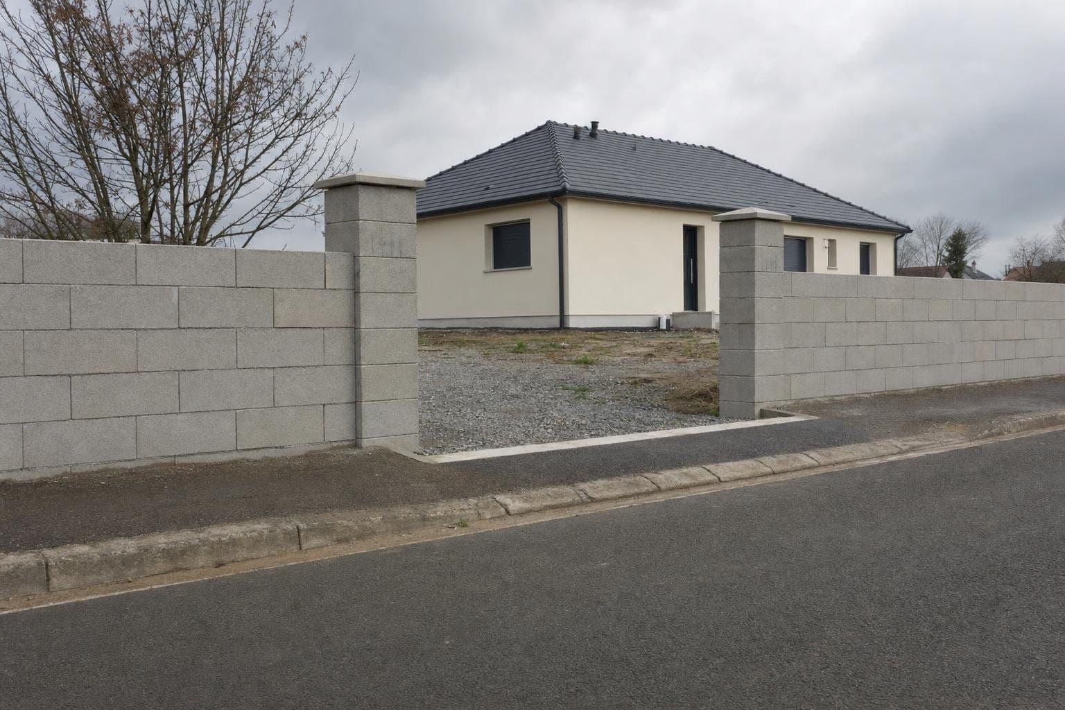 Mur de clôture en blocs béton et piliers de portail maçonnés avec chaperons