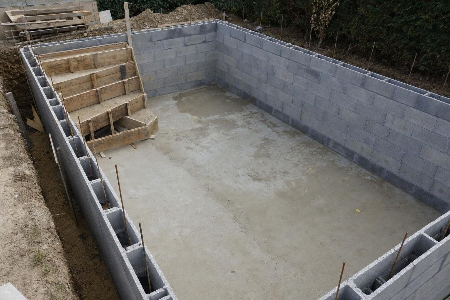 Bassin de piscine en blocs à bancher en construction, radier béton et escalier coffré