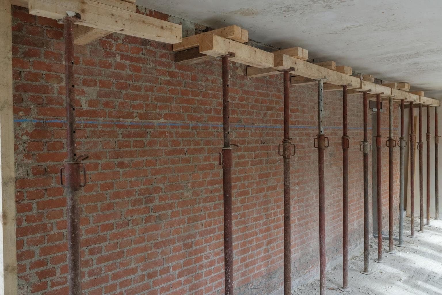 Étais métalliques et bastaings calés sous un plafond le long d'un mur porteur en brique